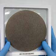 A round polycrystalline diamond plate in a tray, held in gloved hands.
