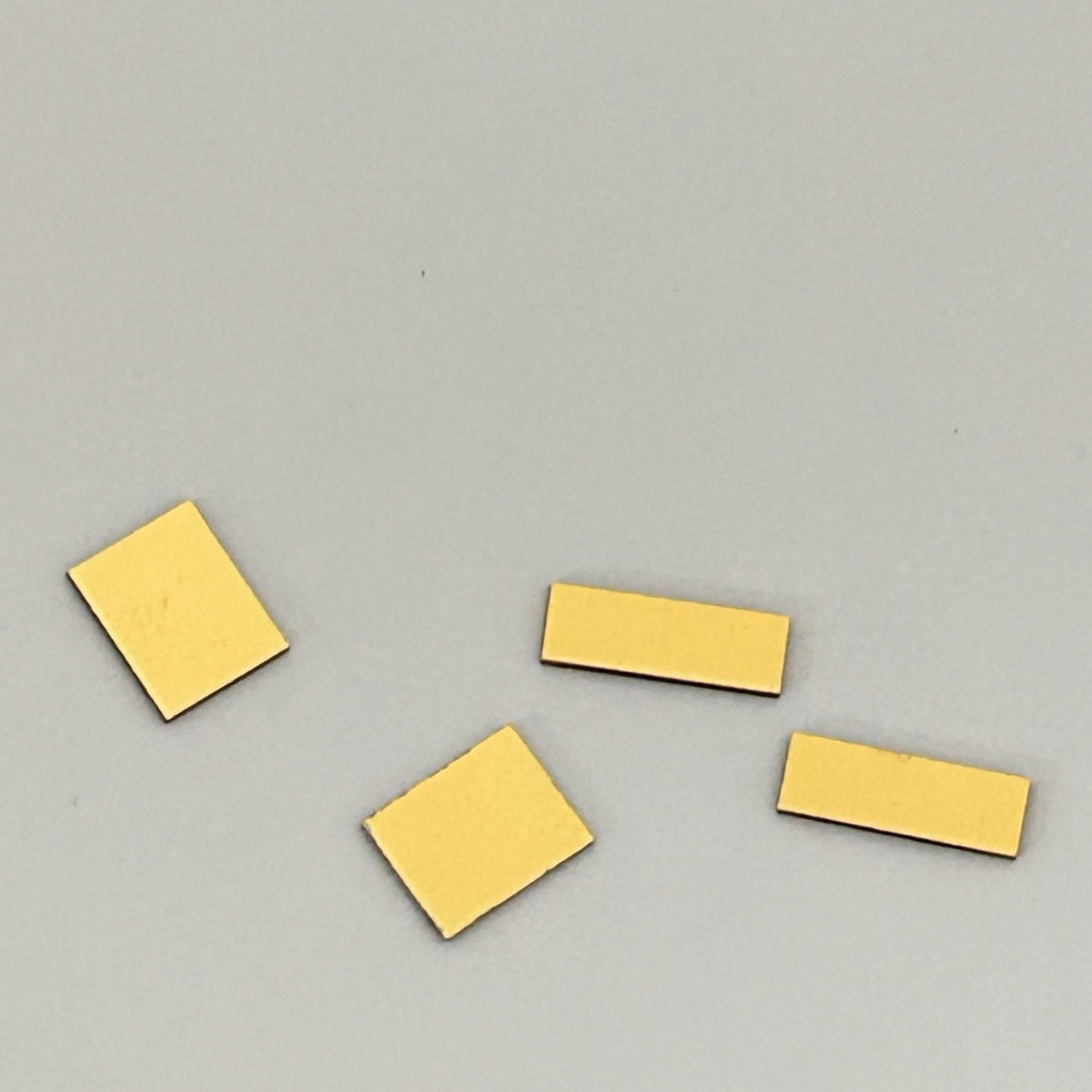 Four gold-coloured metallised single-crystal diamond heat sinks on a grey background.